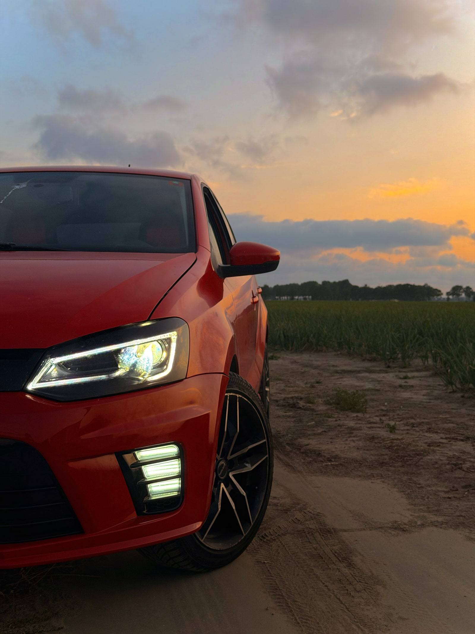Red car at sunset on a sandy track beside a field